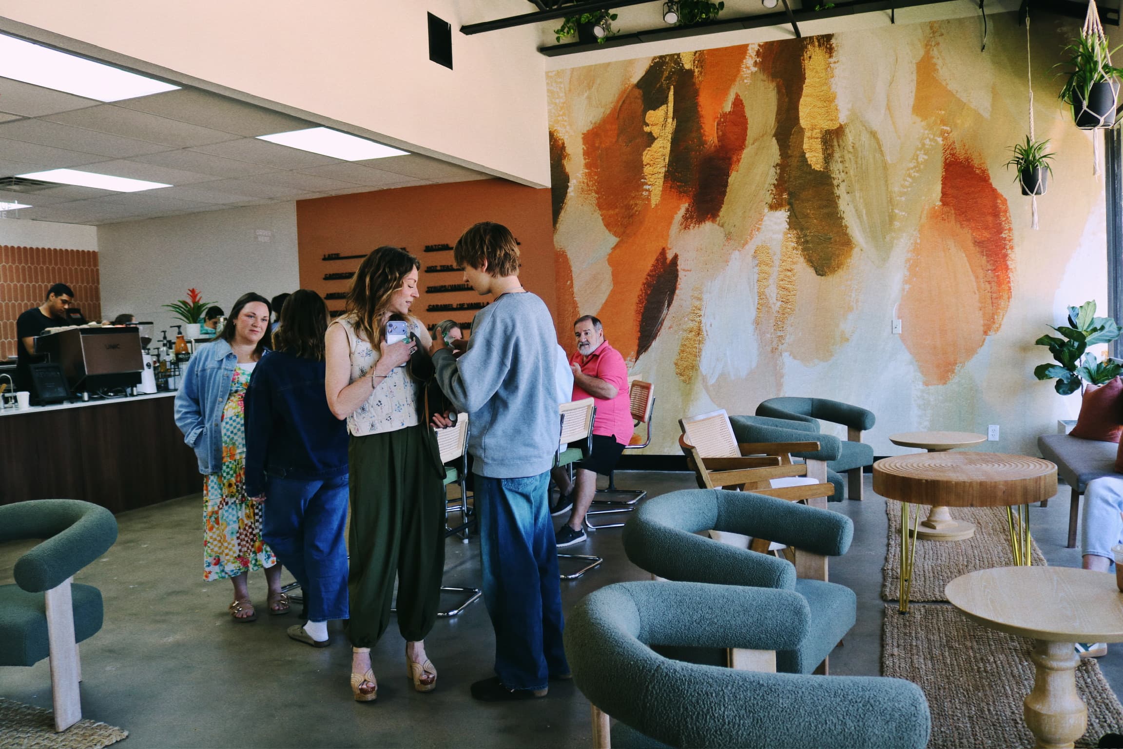Customers chatting near the Revival Coffee counter with the orange-and-cream mural in the background