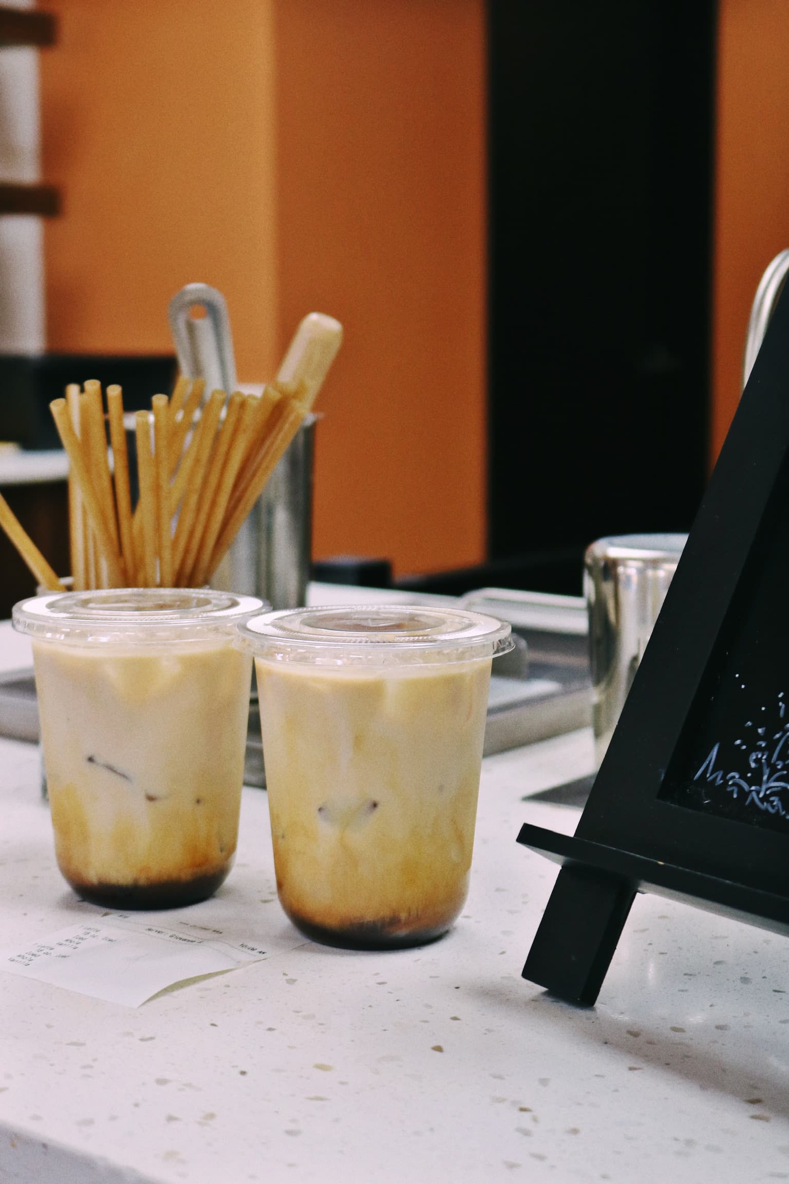 Two iced lattes on the counter beside a stainless steel straw caddy