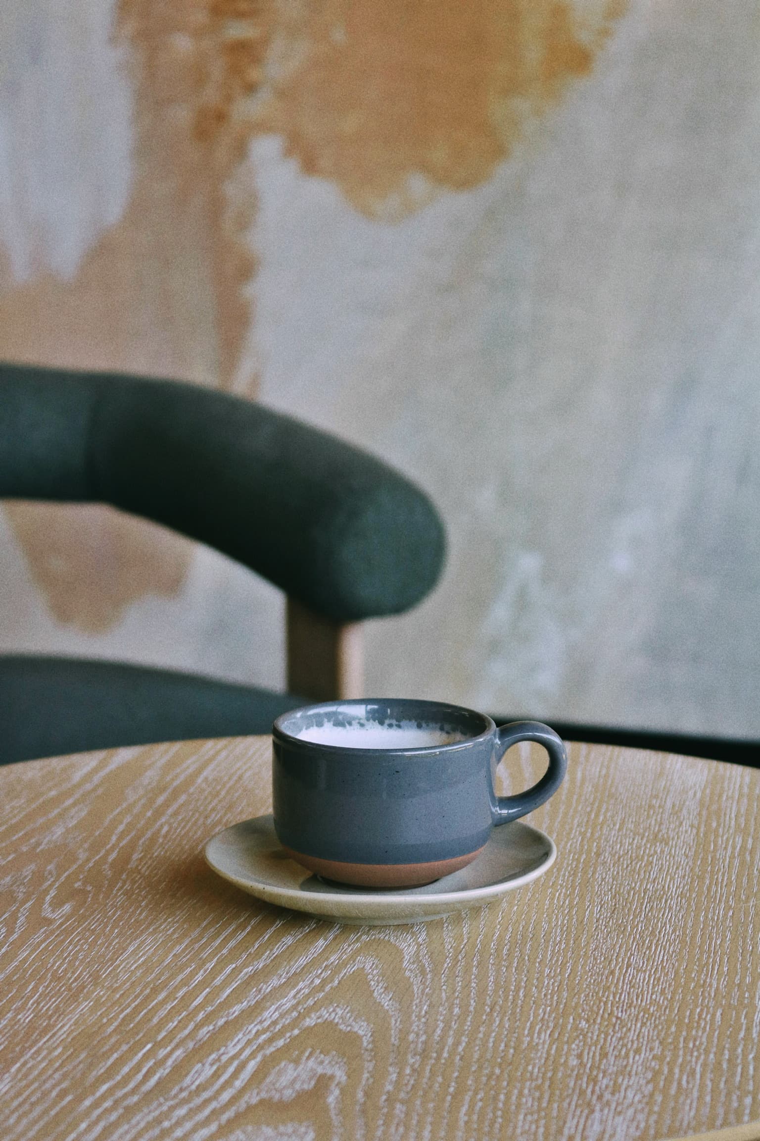 Slate ceramic mug resting on a wood table beside a curved chair