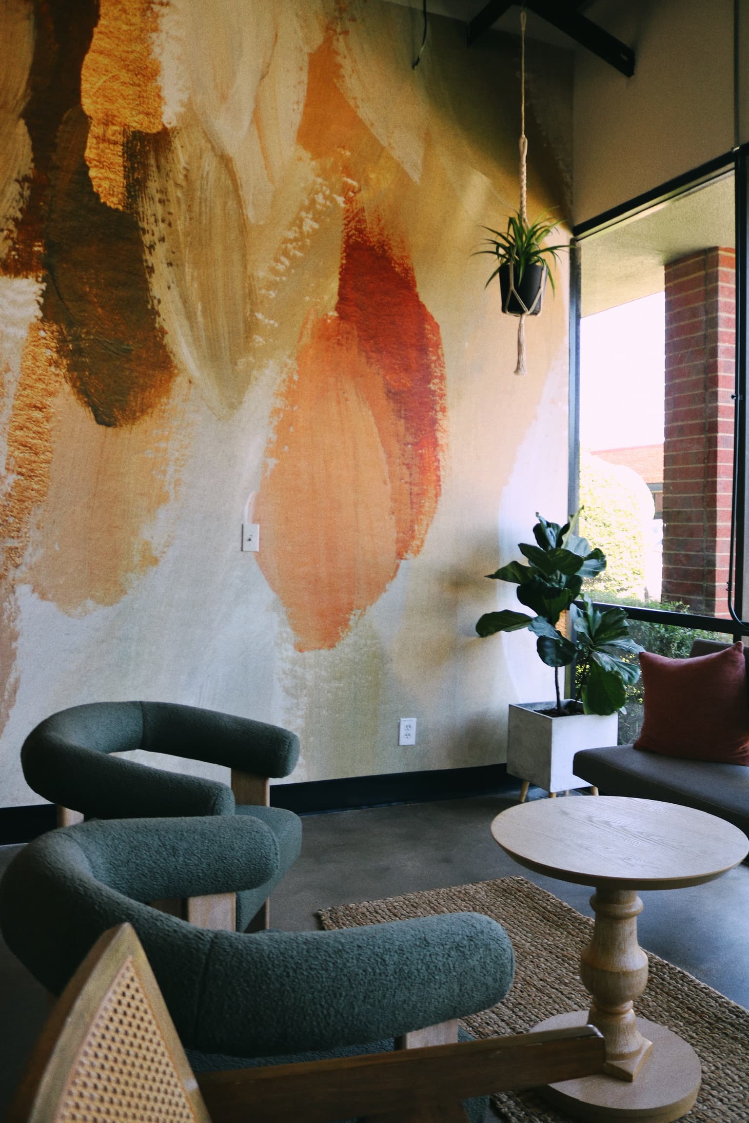 Lounge seating beside the painted feather mural with hanging plants and natural light